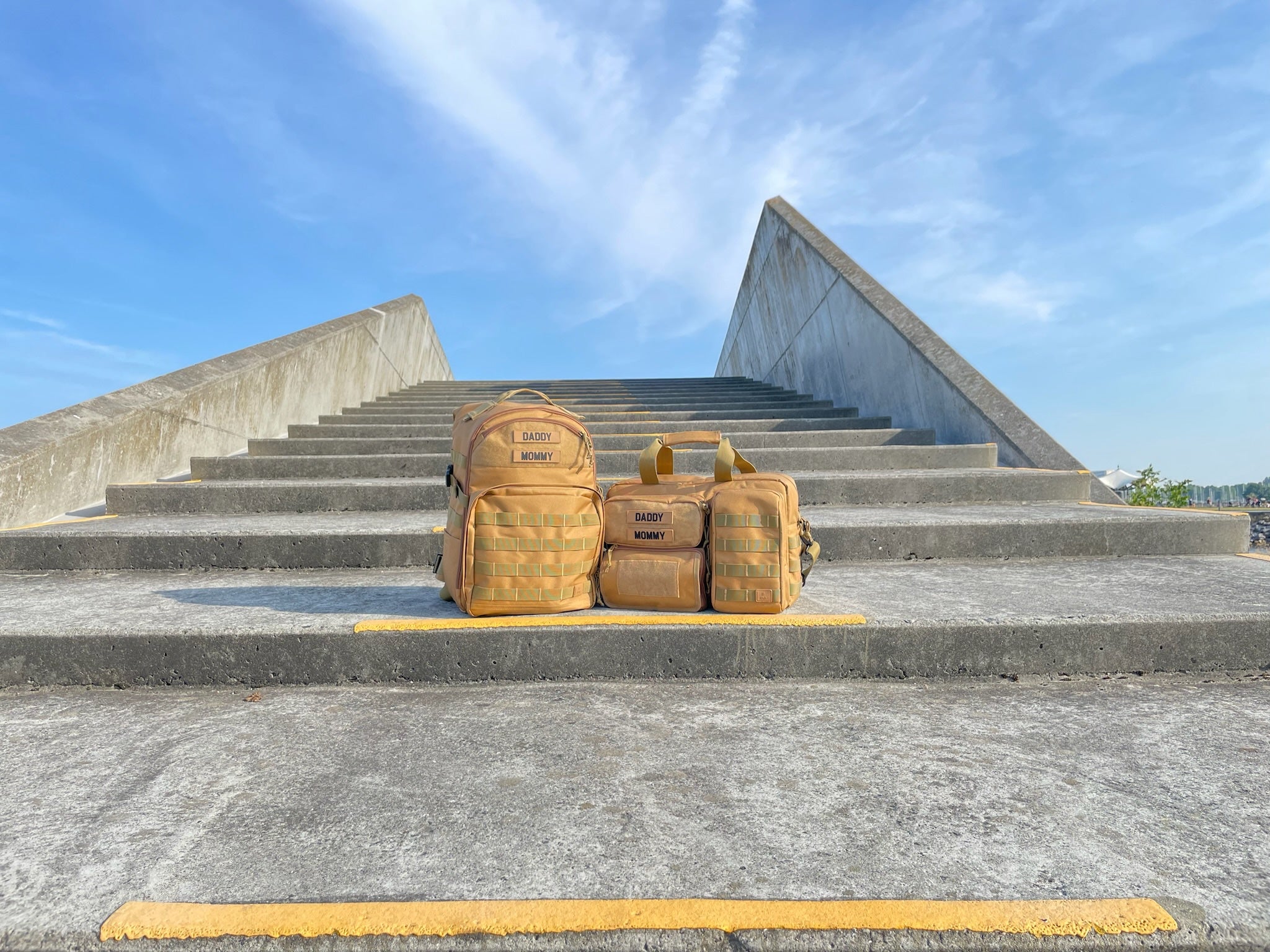 To organiserede pusletasker i farven 'khaki' fra Scandinavianbabygear stående på en betontrappe ved Amagerstrand, København.